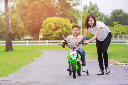 Loving mother help her cute son ride a bicycle.