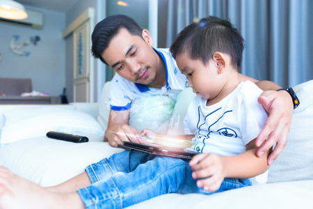 Father and son are using tablet and smiling while spending time together at home.の写真素材