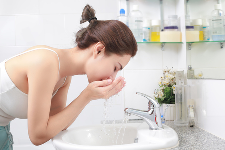 Woman washing her face with water above bathroom sink.の写真素材