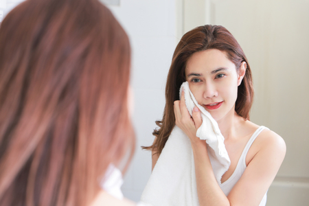 Young woman wiping her face with towel in bathroom.の写真素材