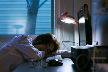 Sleepy exhausted woman working at office desk with her laptop. Overtime working conceptの写真素材