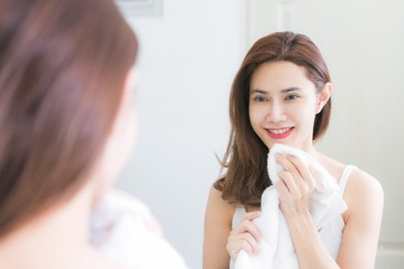 Young woman wiping her face with towel in bathroom.の写真素材