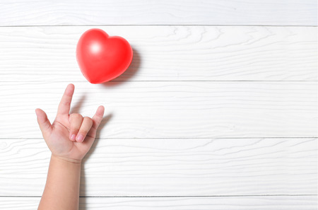 Hand kid supporting love symbol with heart on wooden background.の写真素材