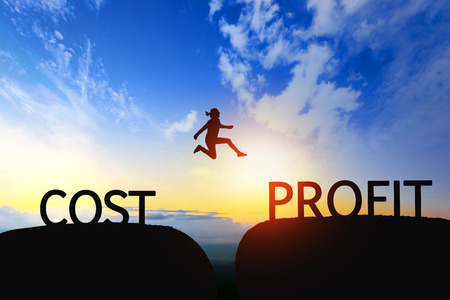 Woman jump through the gap between COST to PROFIT on sunset.の写真素材