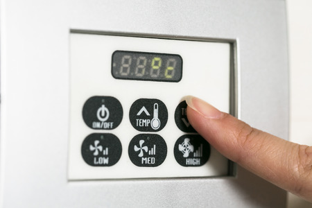 Hand touching screen a hotel thermostat knob to set temperature on energy saving mode.の写真素材