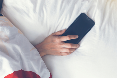 Hand sleeping and holding a mobile phone on the bed. vintage toneの写真素材