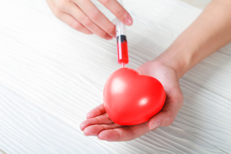 Hand holding plastic Syringe medical injection of red heart. medical conceptの写真素材