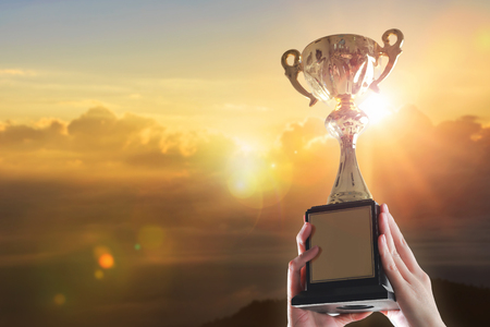 Business hands holding trophy cup on sunset background.の写真素材