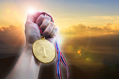 Businessman hand holding golden coin medal on hill.