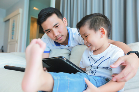 Father and his young son having fun by gaming on a tablet.の写真素材