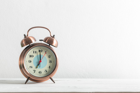 Alarm clock on a white wall and wooden shelf.