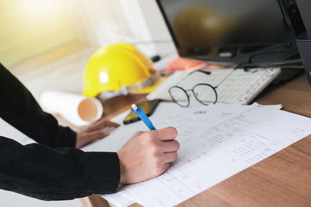 Close-up hand of male architect writing documents on work space wooden table in office.の写真素材