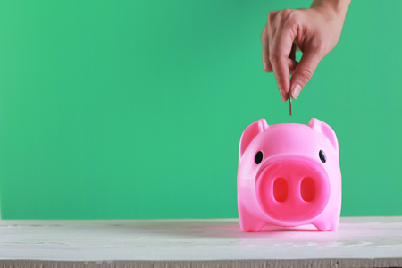 Hand putting a coin into a piggy bank on vintage color background.の写真素材