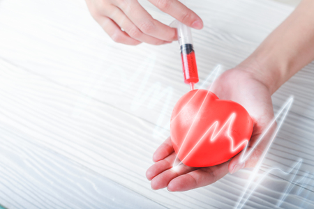 Hands holding plastic Syringe medical injection of red heart. medical conceptの写真素材