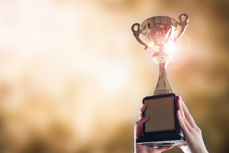 Hands holding trophy cup on gold blurry bokeh background.の写真素材