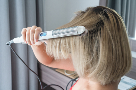 Close-up of a hairdresser straightening gold hair with hair irons.の写真素材