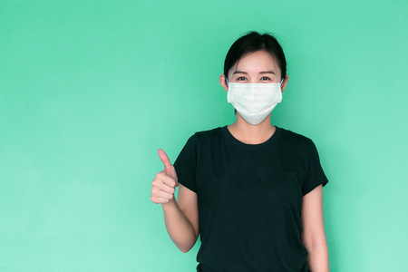 Woman thumb up and wearing protective mask on green background.の写真素材