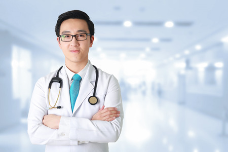 Doctor posing with arms crossed, medical staff working on blurry background.の写真素材