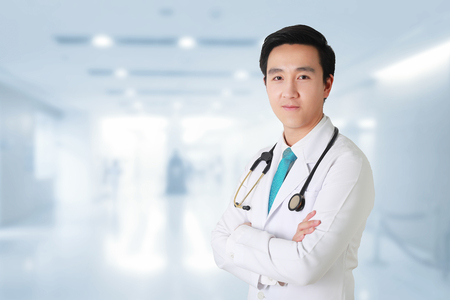Doctor posing with arms crossed, medical staff working on blurry background.の写真素材