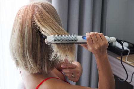 Close-up of a hairdresser straightening long brown hair with hair irons.の写真素材