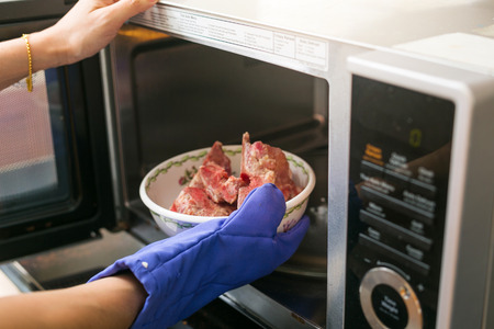 Woman putting grilled pork into microwave oven. inside viewの写真素材