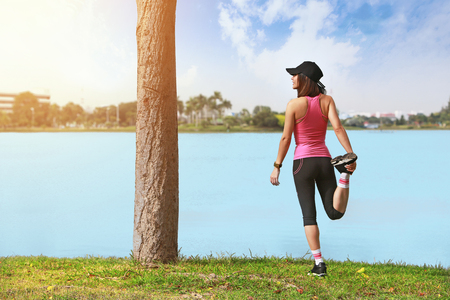 Young fitness woman runner stretching legs before run on park.の写真素材