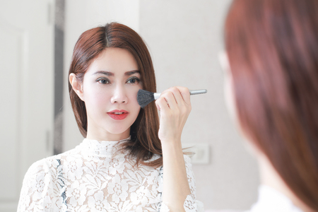 Beautiful young woman applying cosmetic powder on her face with tassel, skin care concept.の写真素材