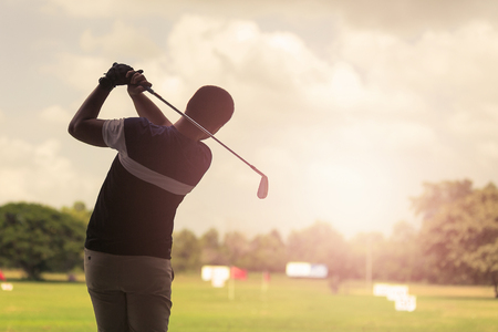 Man hitting golf shot with club on course at evening time.の写真素材