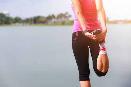 Young fitness woman runner stretching legs before run on park.の写真素材