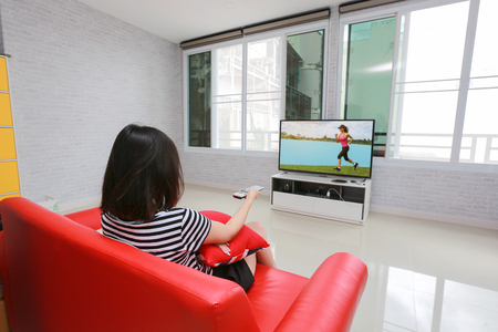 Happy woman watches television while sitting on the sofa.の写真素材