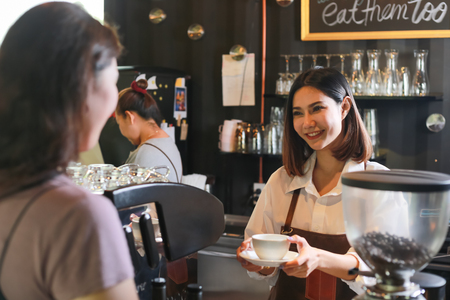 Young female barista serving coffee to customer in cafe.の写真素材
