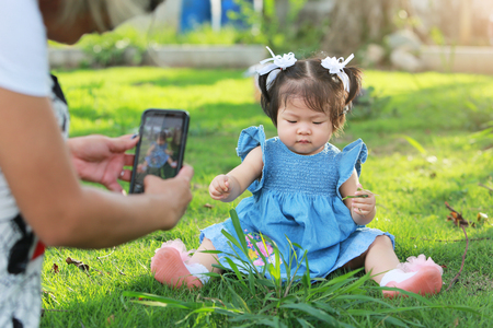 Mother taking a photo with her baby daughter sitting on yard.の写真素材