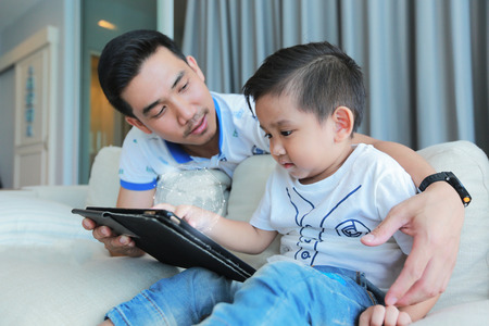 Father and his son happy having fun by gaming on a tablet.の写真素材