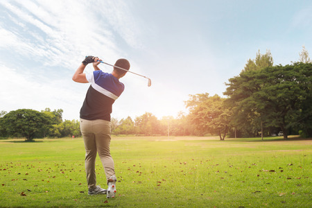 Golfer hitting golf shot with club on course at evening time.の写真素材