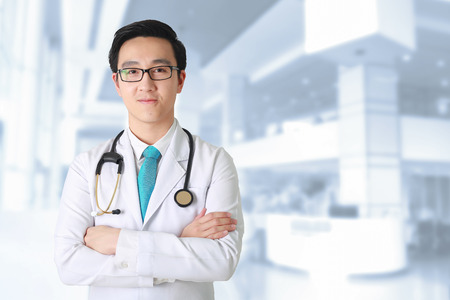 Doctor posing with arms crossed, medical staff working on blurry background.の写真素材