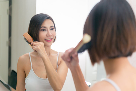 Young asian woman brushing healthy hair in front of a mirror.の写真素材