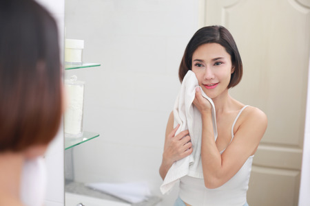 Young asian woman wiping her face with towel in bathroom.の写真素材