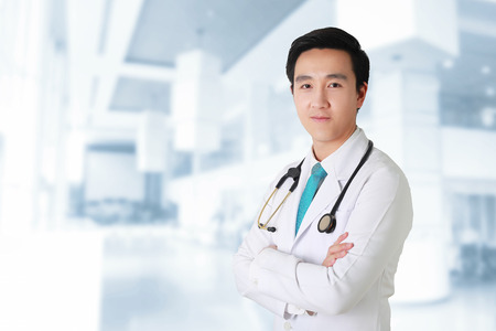 Doctor posing with arms crossed, medical staff working on blurry background.の写真素材