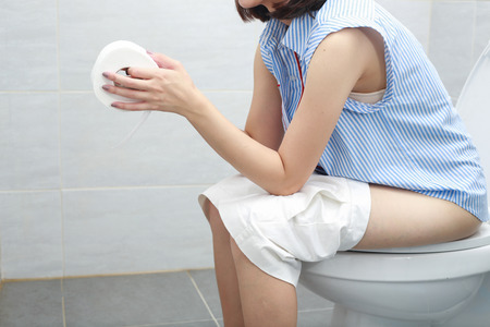 Woman in bath towel sitting on toilet bowl.の写真素材