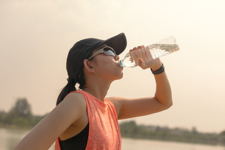 Beautiful fitness athlete woman drinking water after work out exercising on. evening summer.の写真素材