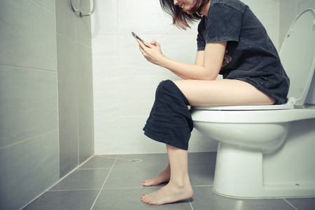 Woman using a smartphone on toilet in morning.の写真素材