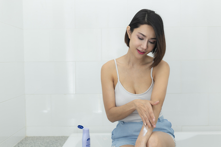 Young woman applying body cream in bathroom.の写真素材