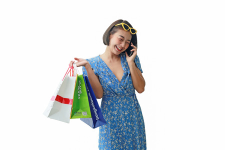 Portrait of smiling woman with colorful shopping bags and calling phone on white background.の写真素材