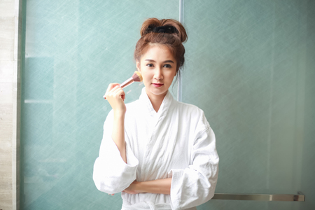 Beautiful young asian woman in bathrobe applying makeup.の写真素材