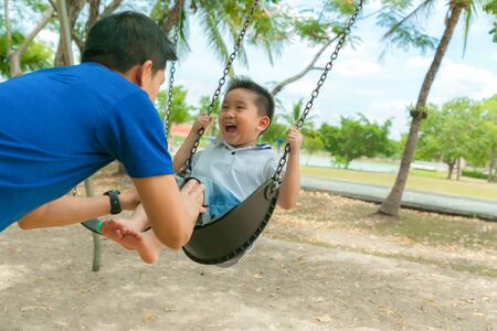 Father and son having funny on swing in playground.の写真素材