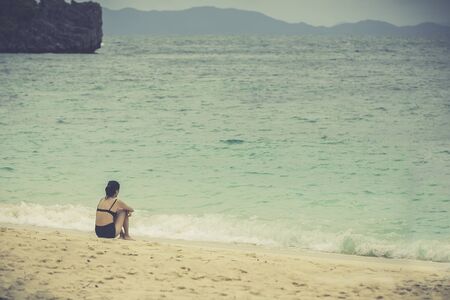 Young woman sitting alone on the beach looking at the sea and sky.の写真素材