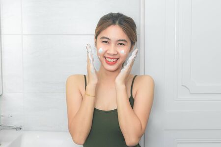 Beautiful young woman washing her face foam in a bathroom.の写真素材