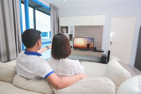 Attractive young asian couple relaxing on a couch at home, watching TV.の写真素材