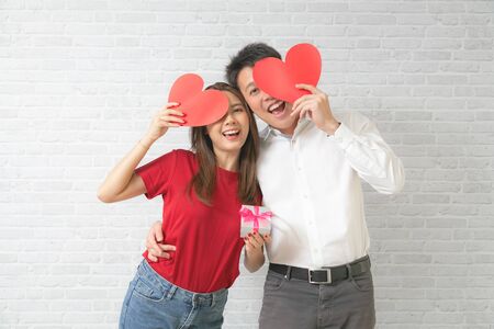 Happy young couple is holding red paper hearts and smiling on blick wall background.の写真素材