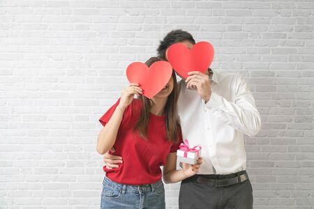 Happy young couple is holding red paper hearts and smiling on blick wall background.の写真素材